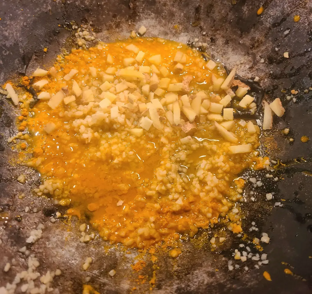 Preparation of neutral oil, turmeric, minced garlic and ginger is shown waiting in the wok for our protein to be added.