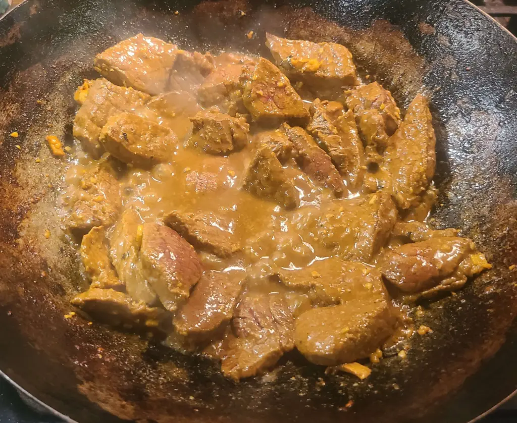London broil slices are stirred in with the oil and turmeric mixture, along with garlic and minced ginger. The wok is just heating up.
