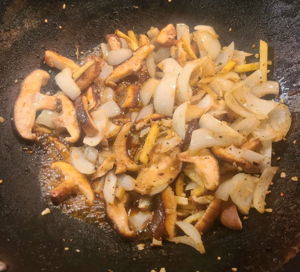 Shiitake mushroom, Vidalia onion, minced garlic, and fresh ginger sticks are shown fried in the wok.