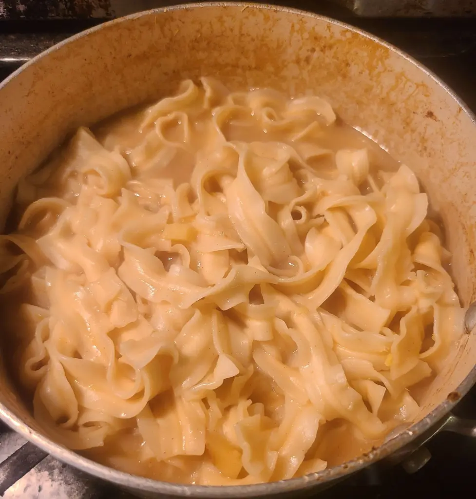 Saucepan full of cooked udon noodles in a now thickened miso reduction.