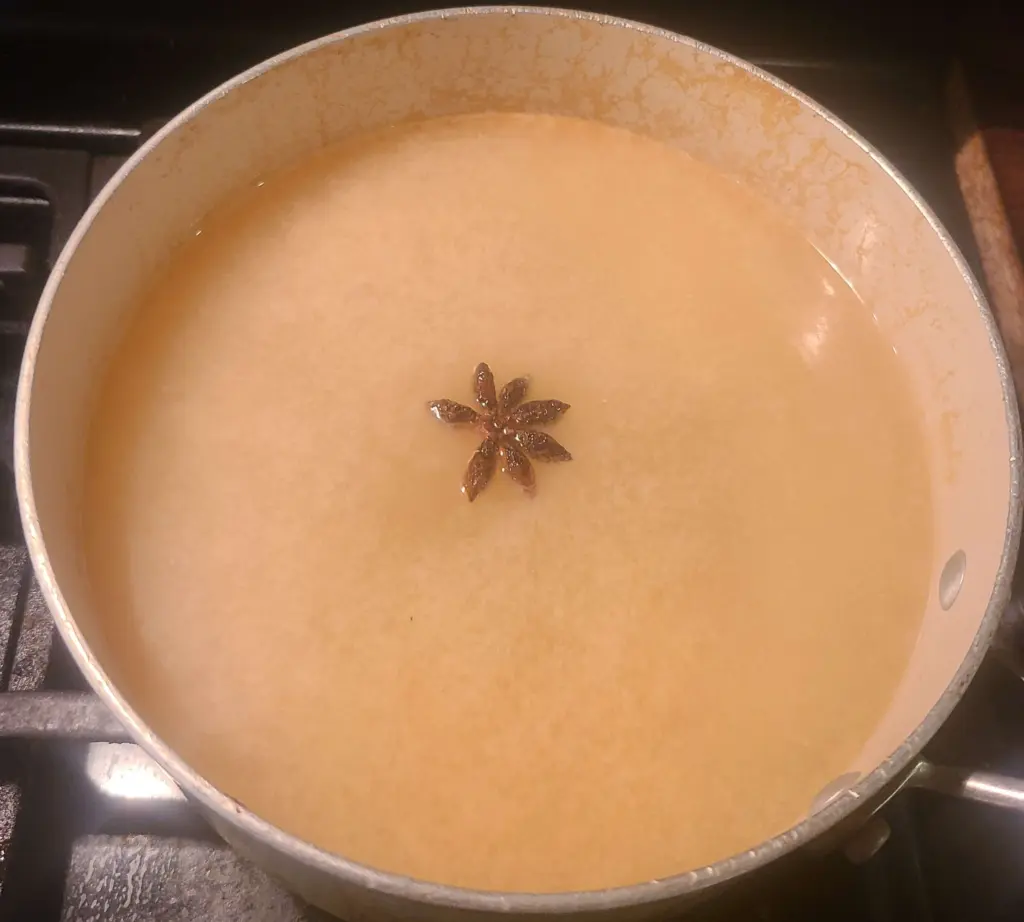 A single star anise floats in a white miso soup broth. The broth is also seasoned with lemongrass, cardamom pods, clove, and cinnamon.